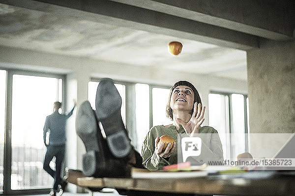 Woman juggling apples in the office sitting with feet on desk