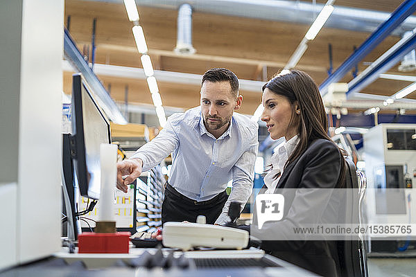Businessman and businesswoman talking at computer in modern factory