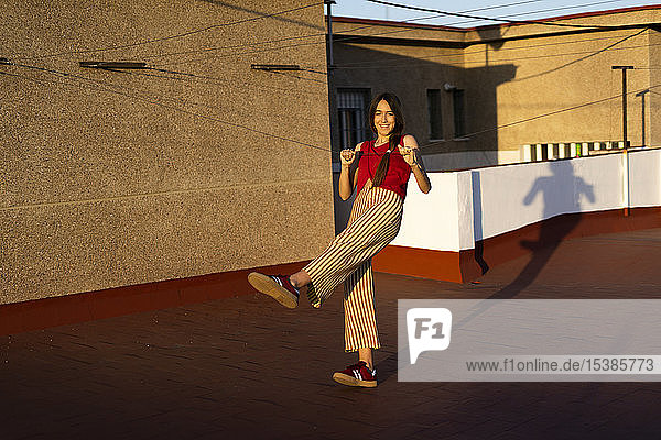 Glückliches Teenager-Mädchen tanzt bei Sonnenuntergang auf der Dachterrasse