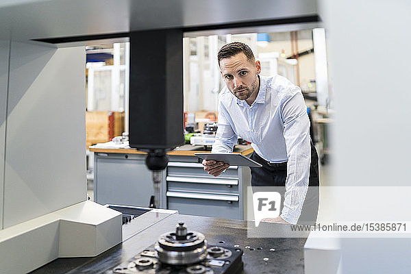 Porträt eines Geschäftsmannes mit Tablette an einer Maschine in einer modernen Fabrik
