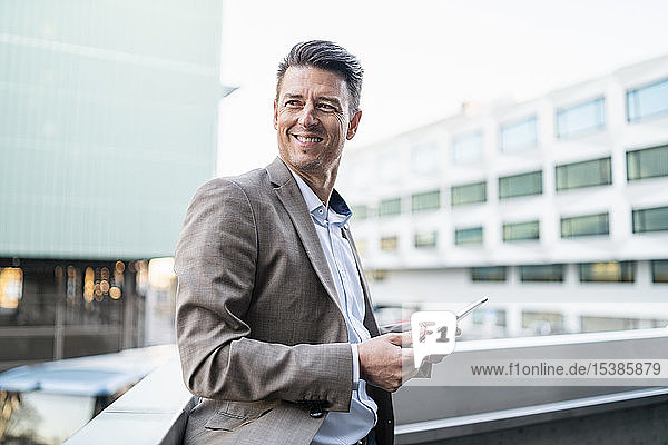 Smiling businessman with tablet on balcony in the city
