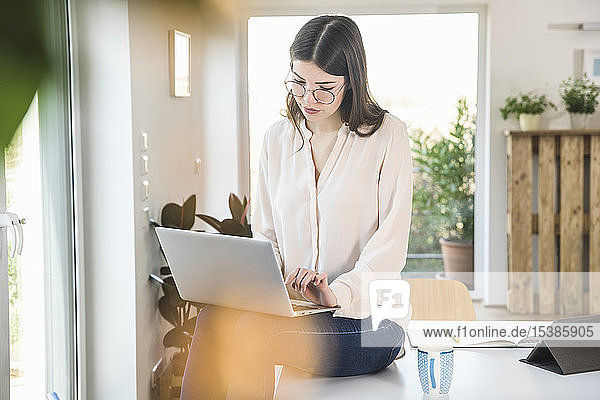 Young woman sitting on table at home using laptop