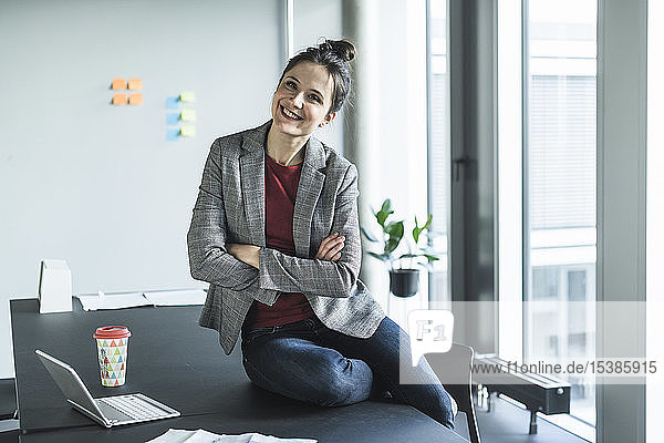 Porträt einer lächelnden Geschäftsfrau  die im Büro auf dem Schreibtisch sitzt