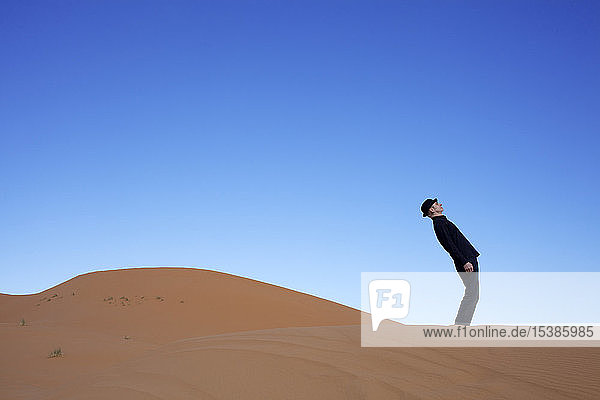 Morocco  Merzouga  Erg Chebbi  man wearing a bowler hat standing crooked on desert dune