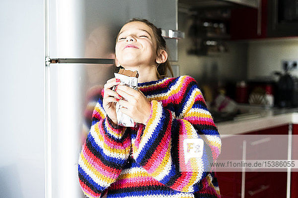 Mädchen in gestreiftem Pullover in der heimischen Küche beim Schokoladenessen