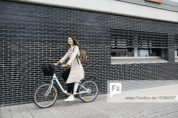 Frau fährt E-Bike entlang einer Ziegelmauer in der Stadt