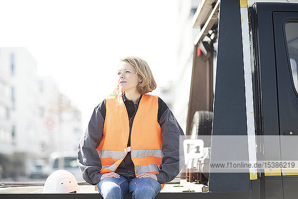 Woman wearing reflective vest sitting on truck platform