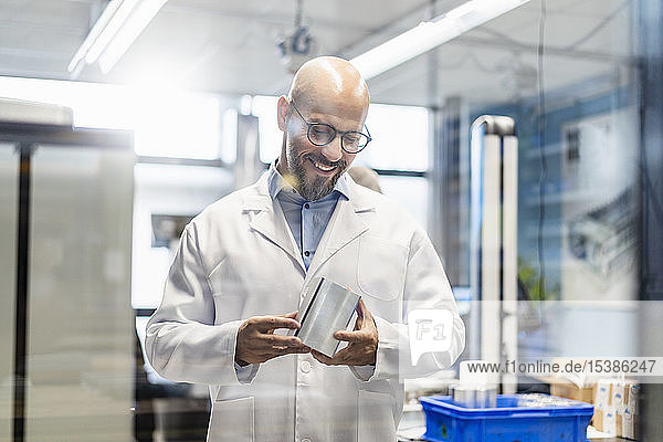 Smiling technician wearing lab coat examining workpiece