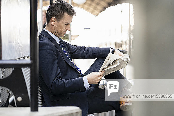 Businessman reading newspaper on station platform