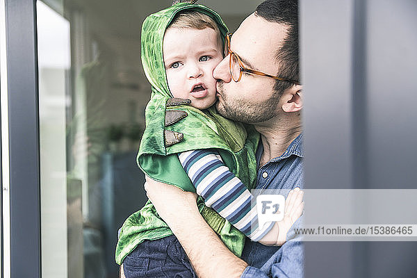 Father kissing son in a costume at terrace door at home