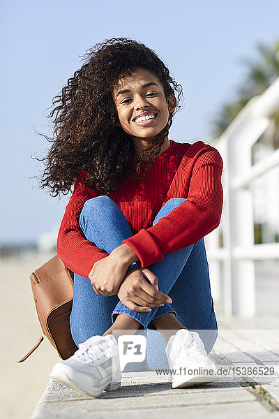 Porträt einer glücklichen jungen Frau  die an der Strandpromenade sitzt