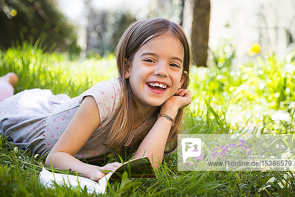 Smiling girl lying on meadow  reading a book