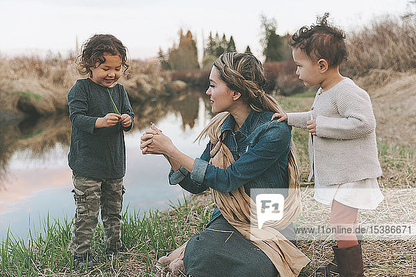 Mutter und Kinder spielen mit einem Grashalm an einem Fluss