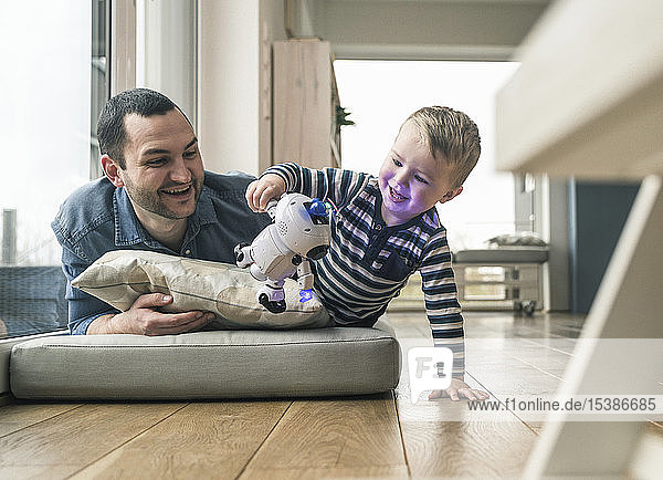 Excited father and son lying on a mattress at home watching a toy robot