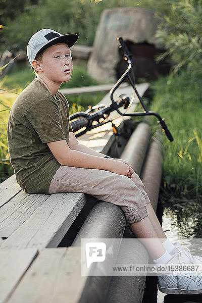 Serious boy woith bmx bike sitting on boardwalk