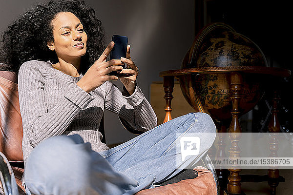 Frau sitzt entspannt im Sessel und benutzt ein Smartphone