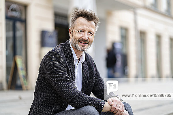 Portrait of smiling mature businessman with greying beard sitting on steps outdoors