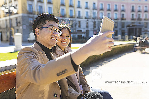 Spain  Madrid  young couple resting on a bench and taking a selfie in the city