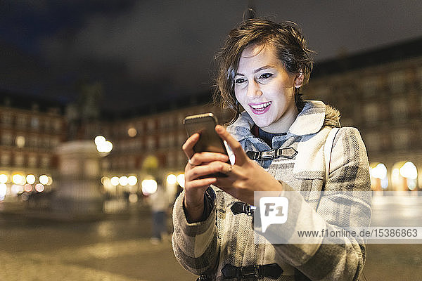 Spanien  Madrid  Plaza Mayor  glückliche junge Frau mit ihrem Smartphone