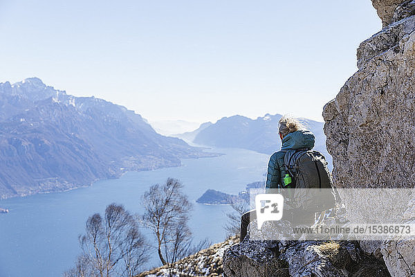 Italien  Como  Lecco  Frau auf Wanderung in den Bergen über dem Comer See  auf einem Felsen sitzend und die Aussicht geniessend