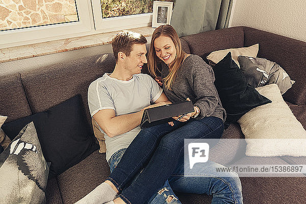 Junges Paar entspannt sich auf dem Sofa und benutzt ein Tablett