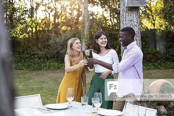 Freunde stoßen bei einem sommerlichen Abendessen im Garten mit Bier an