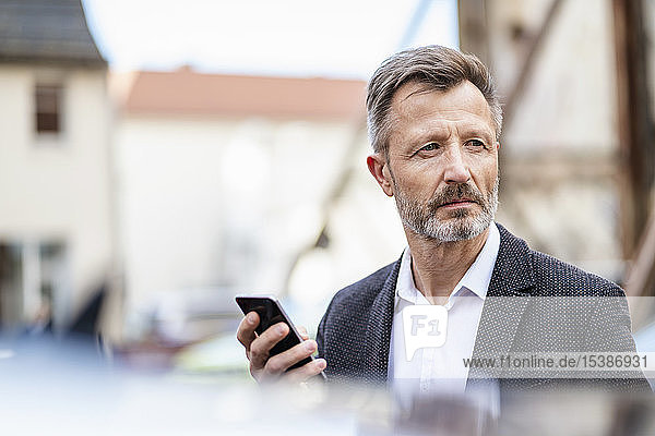 Porträt eines reifen Geschäftsmannes mit Mobiltelefon  der etwas beobachtet