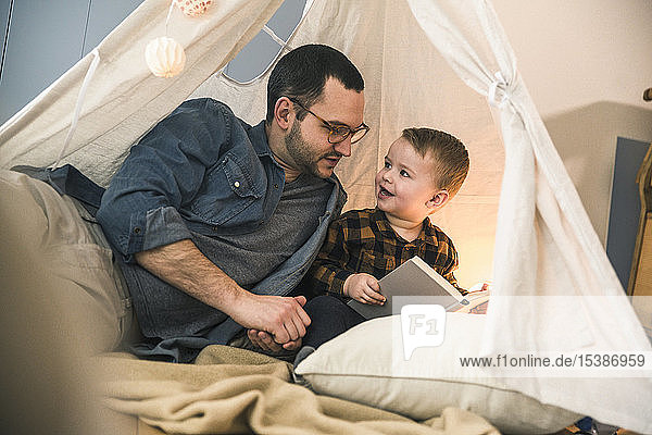 Father and son reading a book together in tent at home