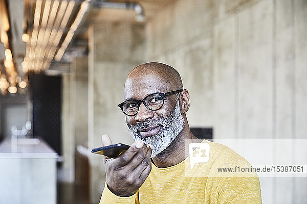 Porträt eines lächelnden reifen Geschäftsmannes  der im Büro ein Smartphone benutzt