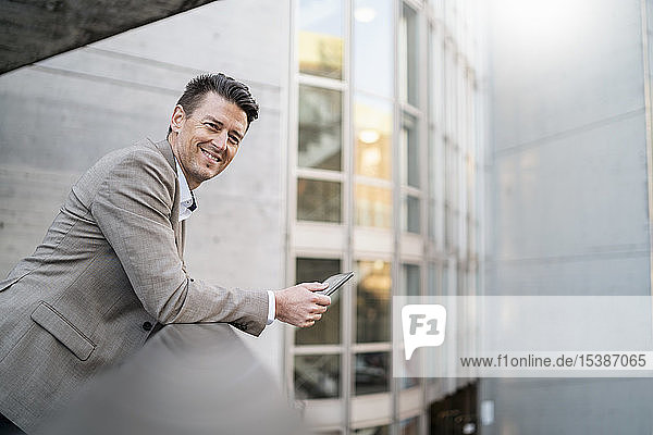 Portrait of smiling businessman with tablet leaning on railing