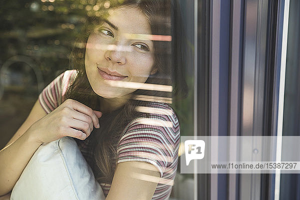 Porträt einer lächelnden jungen Frau hinter einer Fensterscheibe