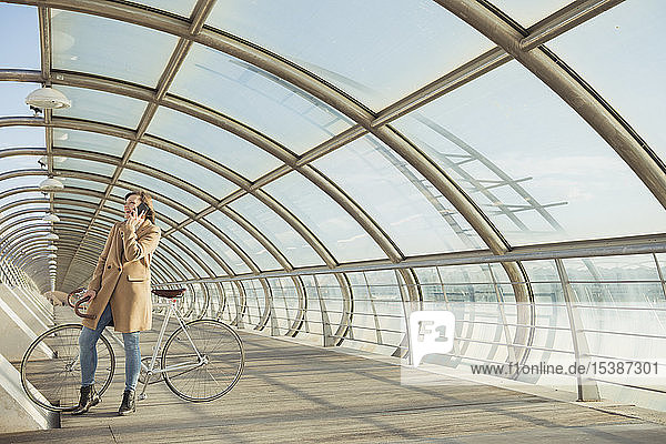 Junge Hipster-Frau mit Fahrrad in einem modernen Tunnel beim Telefonieren