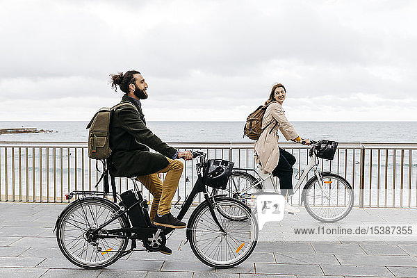 Couple riding e-bikes on beach promenade