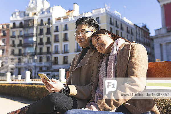 Spanien  Madrid  junges Paar  das sich auf einer Bank ausruht und in der Stadt mobil telefoniert