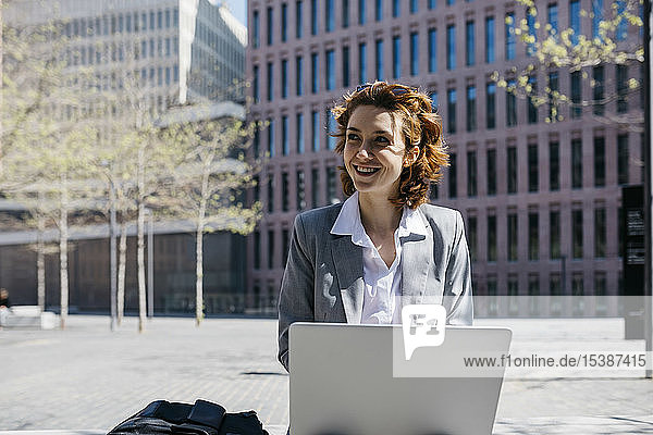 Young businesswoman with red shoes  sitting on a bench in the city  working on laptop