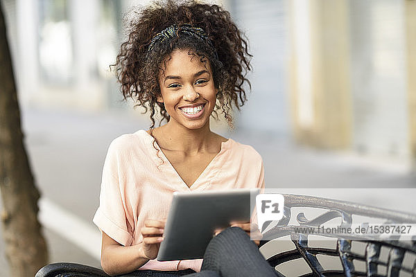 Porträt einer glücklichen jungen Frau  die mit einem Tablett auf einer Bank sitzt