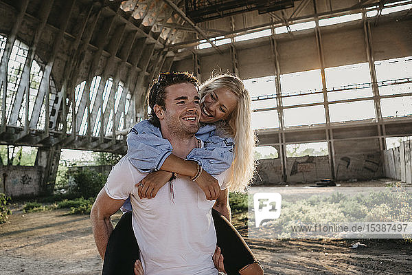 Happy young man giving girlfriend a piggyback ride in an old hall