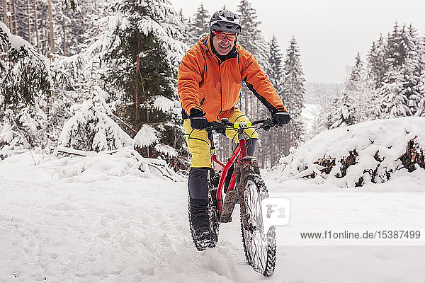 Portrait of happy man riding mountainbike on path in winter forest