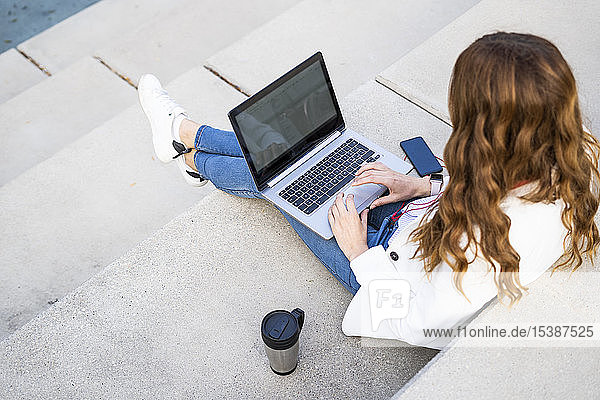 Junge Geschäftsfrau sitzt auf einer Treppe in der Stadt und arbeitet mit einem Laptop