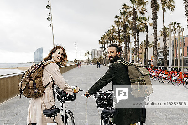 Lächelndes Paar mit E-Bikes an der Strandpromenade