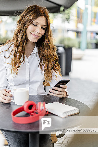 Junge Geschäftsfrau sitzt im Cafe und benutzt ein Smartphone