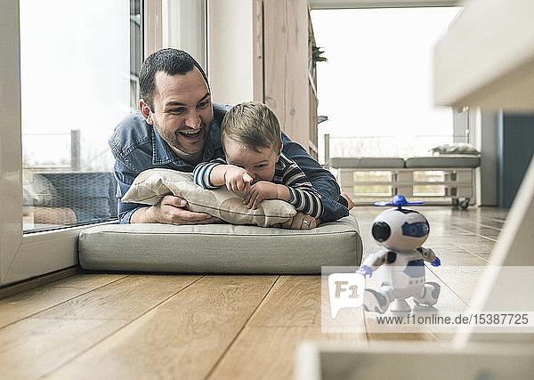 Excited father and son lying on a mattress at home watching a toy robot