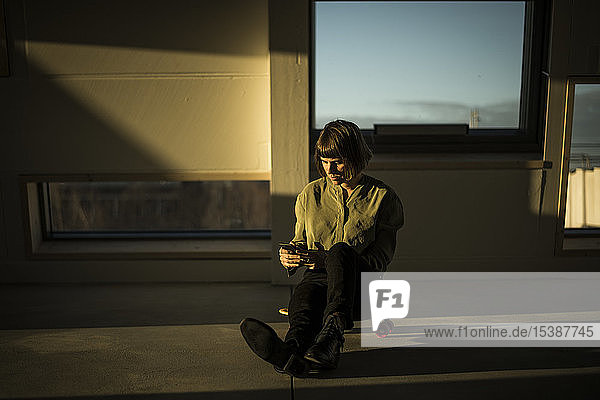 Businesswoman sitting on office floor at sunset  using smartphone