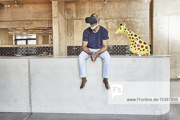 Ein reifer Geschäftsmann im modernen Büro sitzt neben einer Giraffenfigur mit VR-Brille