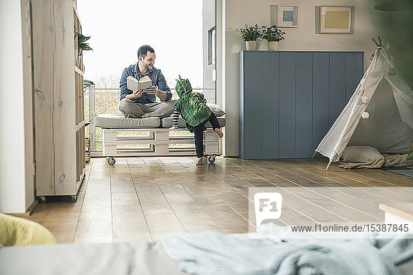 Boy in a costume and father reading book at home