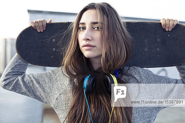 Porträt einer seriösen jungen Frau mit Skateboard und Kopfhörer