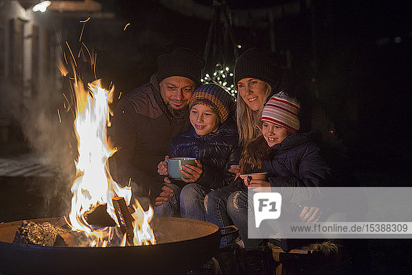 Familie mit Bechern  die nachts am Feuer sitzen