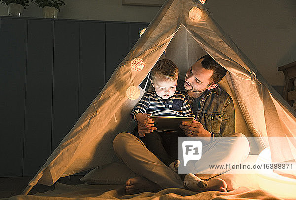 Father and son sharing a tablet in a dark tent at home