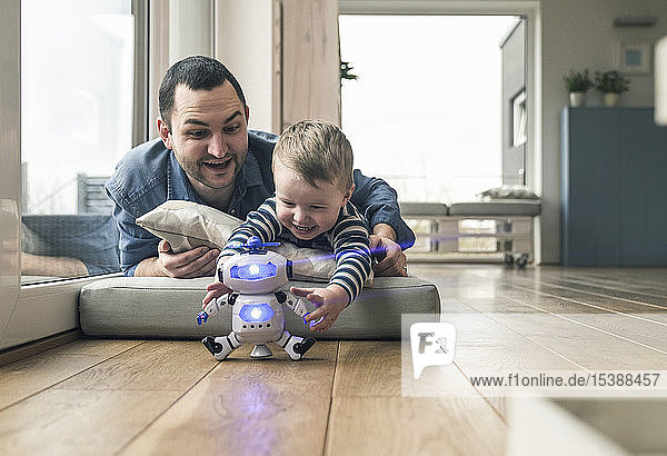 Excited father and son lying on a mattress at home playing with a toy robot