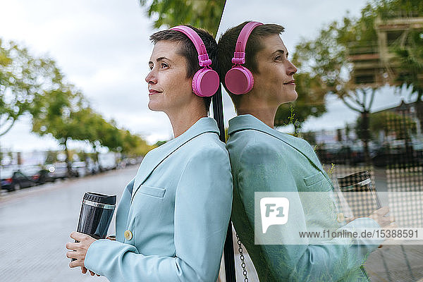 Frau in Jacke mit Thermobecher und rosa Kopfhörer  Reflexion